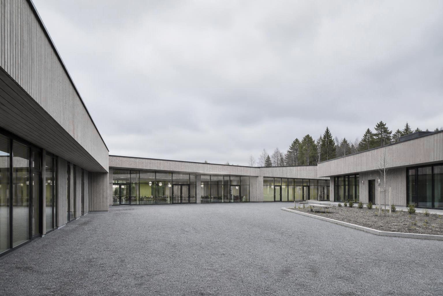 Lav skolebygning i træ og glas, der vinkler sig om et gårdrum i dagslys.
