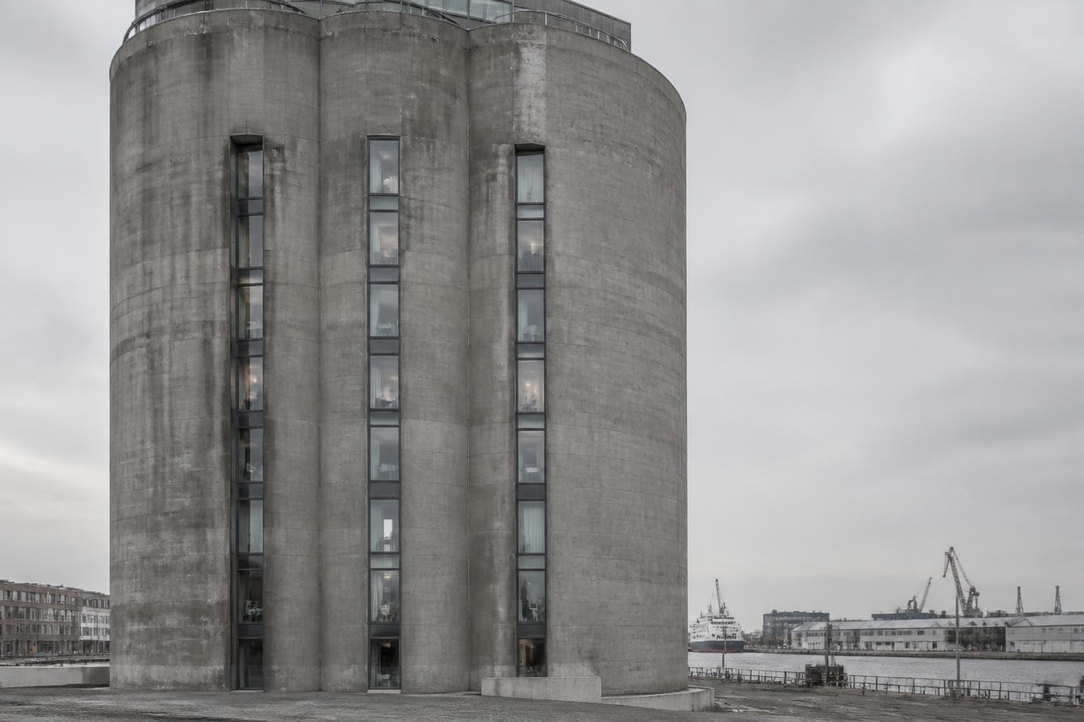 Høj cylindrisk betonsilo med lodrette glaspartier skåret ind i den industrielle betonskal.