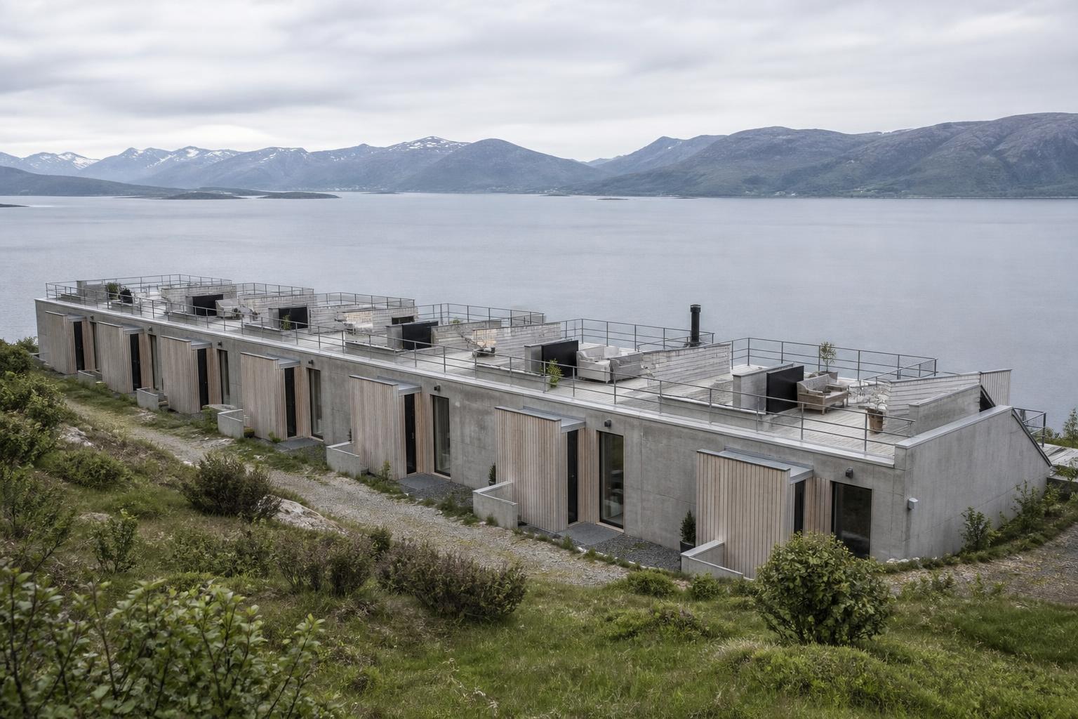Ni terrasserede boliger i beton og træ, trin ned mod en fjord, med fælles tagterrasse.
